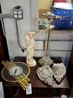 Full view of the lot showing the figurine, lamp base, two marble scroll leaf wall sconces, and the clock on a table.