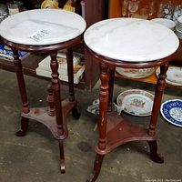 Front side view of the two round marble top plant stands showing wooden legs and bases