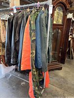 Hanging men's leather jackets, camouflage garment cover, and other jackets on a clothing rack in a warehouse.