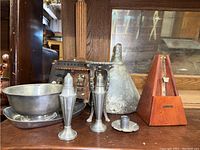 Photo showing pewter salt and pepper shakers, bowl, plate, candle holder, vintage metal funnel, and the wooden metronome on a surface against a mirror reflection.