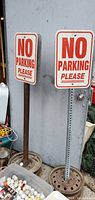 Two metal No Parking Please signs on stands shown against a wall with some items around.