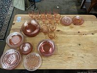 Top view of pink carnival glass dishes, bowls, mugs and stemware displayed on wooden table