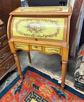 Full view of the roll top desk showing the floral design on the roll top and drawer fronts, featuring tapered legs and overall decorative style.