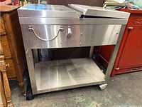 Front view of stainless steel portable sink cart showing surface, handles, closed lid, and casters.
