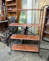 Front view of four-tier metal frame shelf with wooden shelves, showing scratches and scrapes on wood and decorative metal ends.
