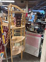 Photo showing wooden corner shelf unit with four tiers and a small black floral jewelry box on second shelf, Gerry baby gate packaging leaning beside it.