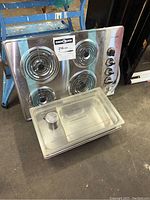 Commercial stainless steel food storage rectangular container with fitted lid and small perforated insert inside, shown beside the stove top.