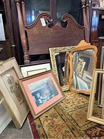 Five framed pieces displayed leaning against furniture: statuette shadow box, watercolor, photo print, and two framed mirrors.