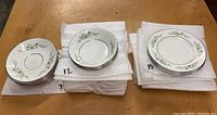 Stack of 7 saucers, 12 bowls, 10 plates all with green floral pattern and silver rim