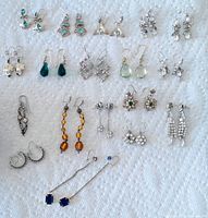 Full display of 18 pairs of vintage earrings laid out on a white textured fabric, showing variety in shape, color, and style, mostly in silver-tone with colorful stones.
