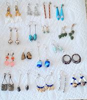 Photo showing 18 pairs of vintage pierced earrings arranged on a white cloth, variety of styles and colors