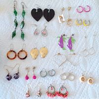Top view showing all 18 pairs of vintage pierced earrings in assorted styles and colors laid on a white textured surface.