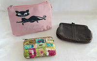 Three vintage change purses together on white surface: pink vinyl cat purse, patchwork purse, brown leather purse