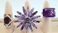 Three vintage purple statement rings displayed on a beige ring stand, showing bulk lot contents and style variety.
