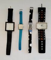 Four vintage watches laid flat in a row, showing different designs of watch faces and bands