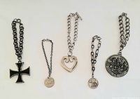 Five charm bracelets laid out showing chains and pendants including cross, heart, round charms with text and detailed designs.
