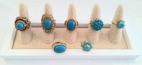 Full view of all seven vintage chunky blue statement rings on a beige display stand, showing the variety in stone shapes and settings.