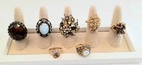 Full view of seven vintage multi-color cocktail rings displayed on ring holders, showing variety of colors and designs.