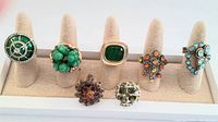 Seven vintage multi-color statement rings arranged on fabric finger stands in white tray, front view