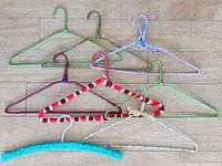 Top down view of 8 wrapped and crocheted vintage wire hangers in different colors and patterns arranged on a wooden surface.