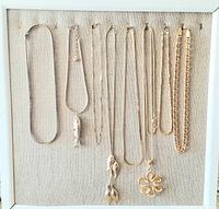 Eight vintage necklaces arranged on a beige fabric board showing variety of chains and pendants.