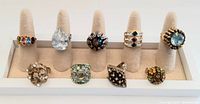 Front view of 9 vintage cocktail rings arranged on ring display stand showing varied colorful stones and metal designs.