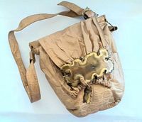 Front view of the vintage beige handbag showing the flap with metal decorative piece and shoulder strap