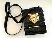 Photo of the vintage black handbag showing the front with croc pattern and gold tiger head detail on flap along with an adjustable shoulder strap.