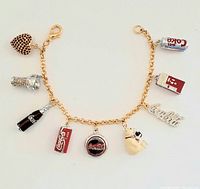 Full view of gold-tone charm bracelet with 9 Coca-Cola themed charms, laid flat.