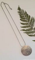 Full view of silver chain necklace with round engraved brooch attached, showing length and overall condition.