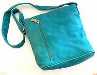 Photo of turquoise shoulder handbag showing front with zipper pocket and adjustable strap.