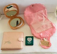 Top view of various pink vinyl and plastic vintage 1960s accessories including a compact mirror, accessory bags, and a set of travel clothes line clips.