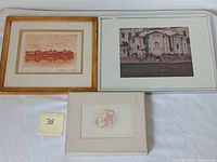Three framed artworks arranged side by side showing lithograph, photograph, and intaglio art prints on a white cloth background with lot number marker