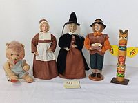 Front view of 5 figurines including a bear-like doll, female pilgrim, witch, male caroler, and Annalee doll