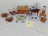 Full view of miniature dollhouse furniture and porcelain tea sets arranged on white surface with a yellow post-it note number 10