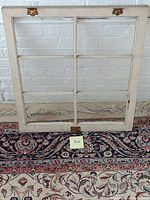 Vintage wooden window frame painted white with six rectangular glass panes. One pane is visibly cracked near the center bottom.