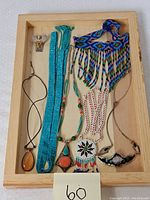 Entire lot of necklaces and pendants arranged in wooden tray for full view.