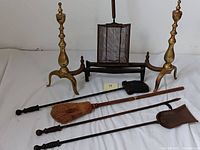 Side view of the vintage fireplace tool set including brooms, shovel, poker, brass andirons, and popcorn basket
