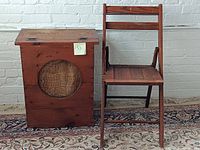 Side by side view of wooden folding chair and wooden speaker box in front of white brick wall on patterned rug