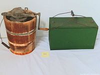 Side view of vintage wooden crank ice cream maker and green metal chest cooler showing detached wooden bucket handle and metal crank lid on ice cream maker, and handle and latch on cooler.
