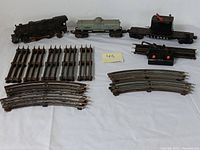 Vintage Lionel train set including locomotive, freight car, coal tender, straight and curved tracks, and power supply on white background.