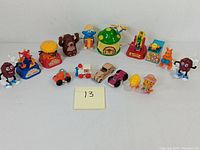 Full shot showing all 13 miniature windup toys including California Raisins figures, windup rides, Smurfs, cars, and animal figures on white background.