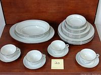 Full set arranged showing cups stacked with their saucers, plates, casseroles and platter behind in neat organized piles.