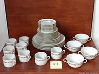Full set stacked including 8 teacups in front, 4 soup bowls with handles on the right, various plates stacked centrally showing size gradation and florals with gold rims