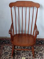 Front view showing vertical spindles, curved armrests, contoured wooden seat and turned legs with rockers.