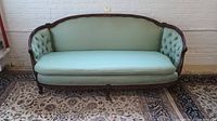 Front view of vintage fabric-upholstered sofa with carved wood frame, light green color, tufted armrests, and smooth seat cushion.