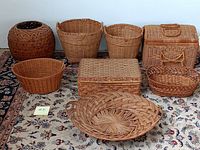 Photo showing the collection of nine vintage wicker baskets of various sizes and shapes displayed on a patterned rug, for harvesting and storage.