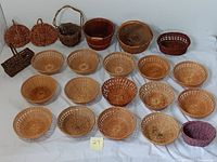 Top view of 17 round shallow wicker baskets, mostly light brown with one purple-dyed basket, arranged on a white surface.