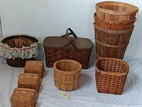 Photo showing all nine baskets in the lot arranged together, highlighting mix of shapes, sizes, and types including tall wooden, small square wicker, lace-trimmed, and picnic baskets.