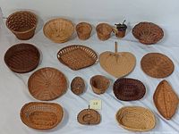 Top view of 18 wicker baskets arranged on a white surface showing varying sizes, shapes, and colors from natural light wicker to dark brown.